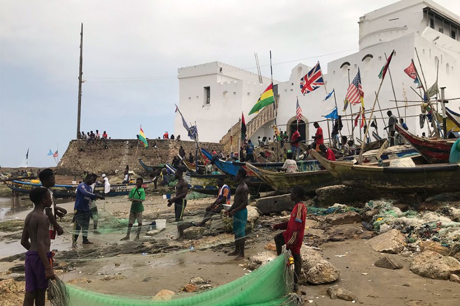 Fishermen in front of Cape Coast Castle, Ghana, with a staircase on the left leading up to a ‘Door of No Return’.