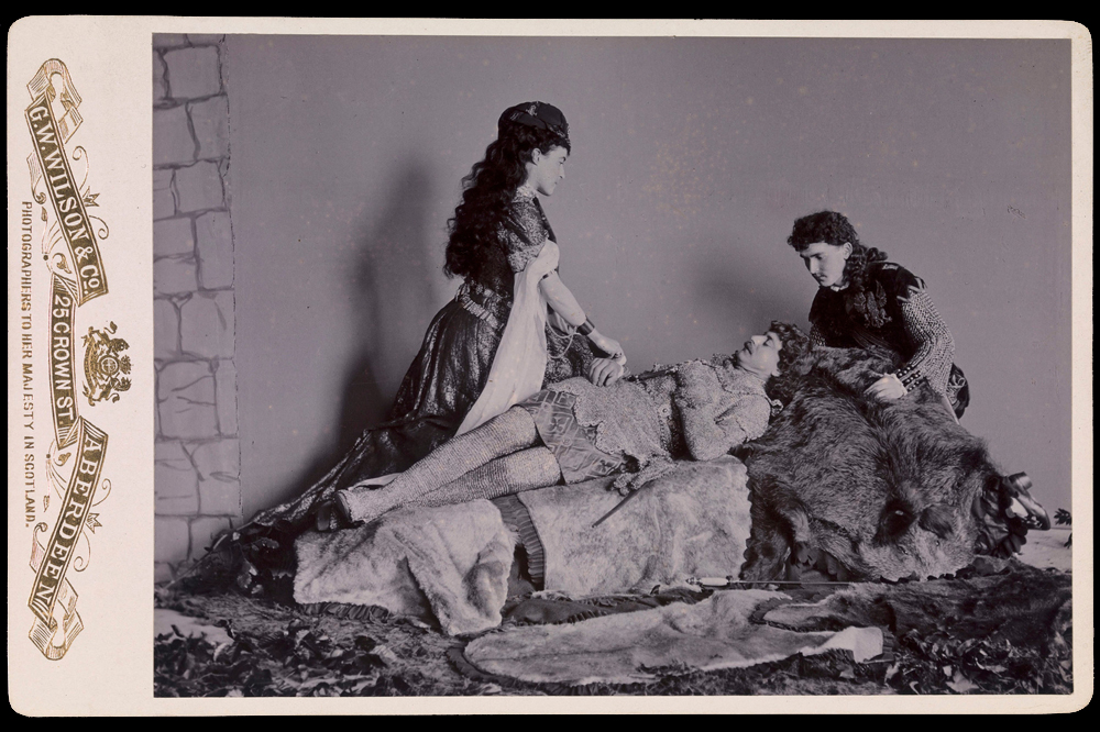 Photograph taken at Balmoral in 1893/94 by Charles Albert Wilson. Ethel Cadogan, Lord William Cecil and Dr Alexander Profeit re-enact a scene from Ivanhoe by Sir Walter Scott in which Rebecca and a page kneel over Ivanhoe. Royal Collection Trust/© HM Queen Elizabeth II 2020