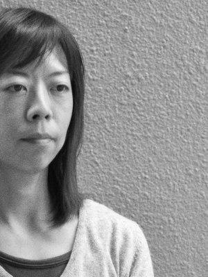black and white photograph of a Japanese woman standing against a textured wall