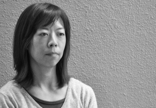 black and white photograph of a Japanese woman standing against a textured wall