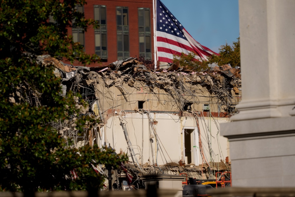 A US flag flies in the background as the ruins of the facade of the East Wing can be seen in the foreground
