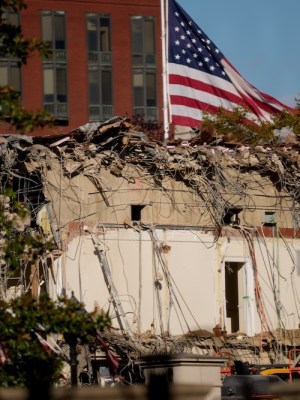 A US flag flies in the background as the ruins of the facade of the East Wing can be seen in the foreground