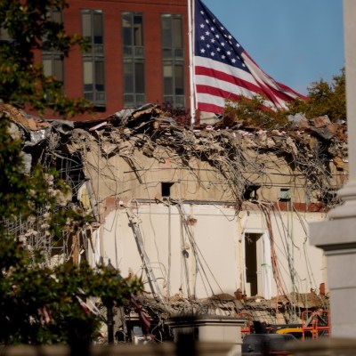 A US flag flies in the background as the ruins of the facade of the East Wing can be seen in the foreground
